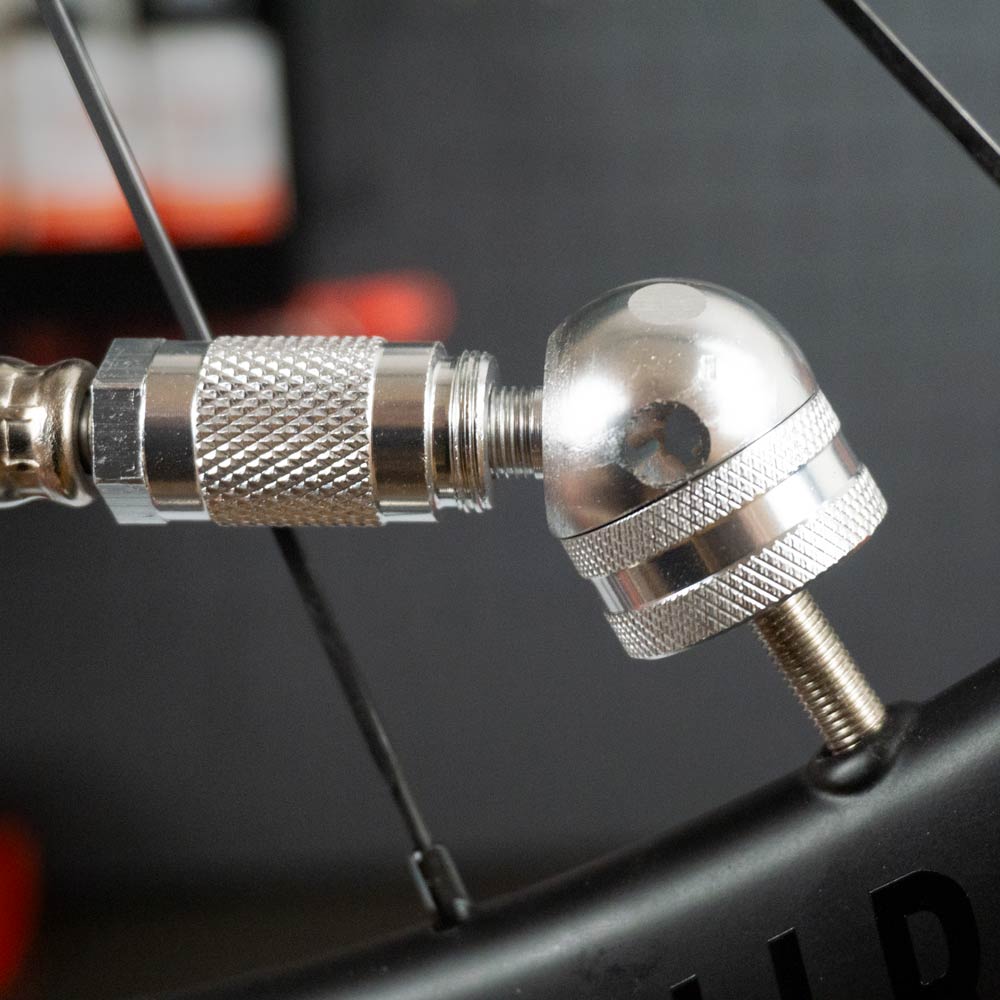 Close-up of the Prestacycle Big Angle Presta Head attached to a tubeless valve on a bicycle wheel, showcasing the detailed texture and shiny finish of the metal components.