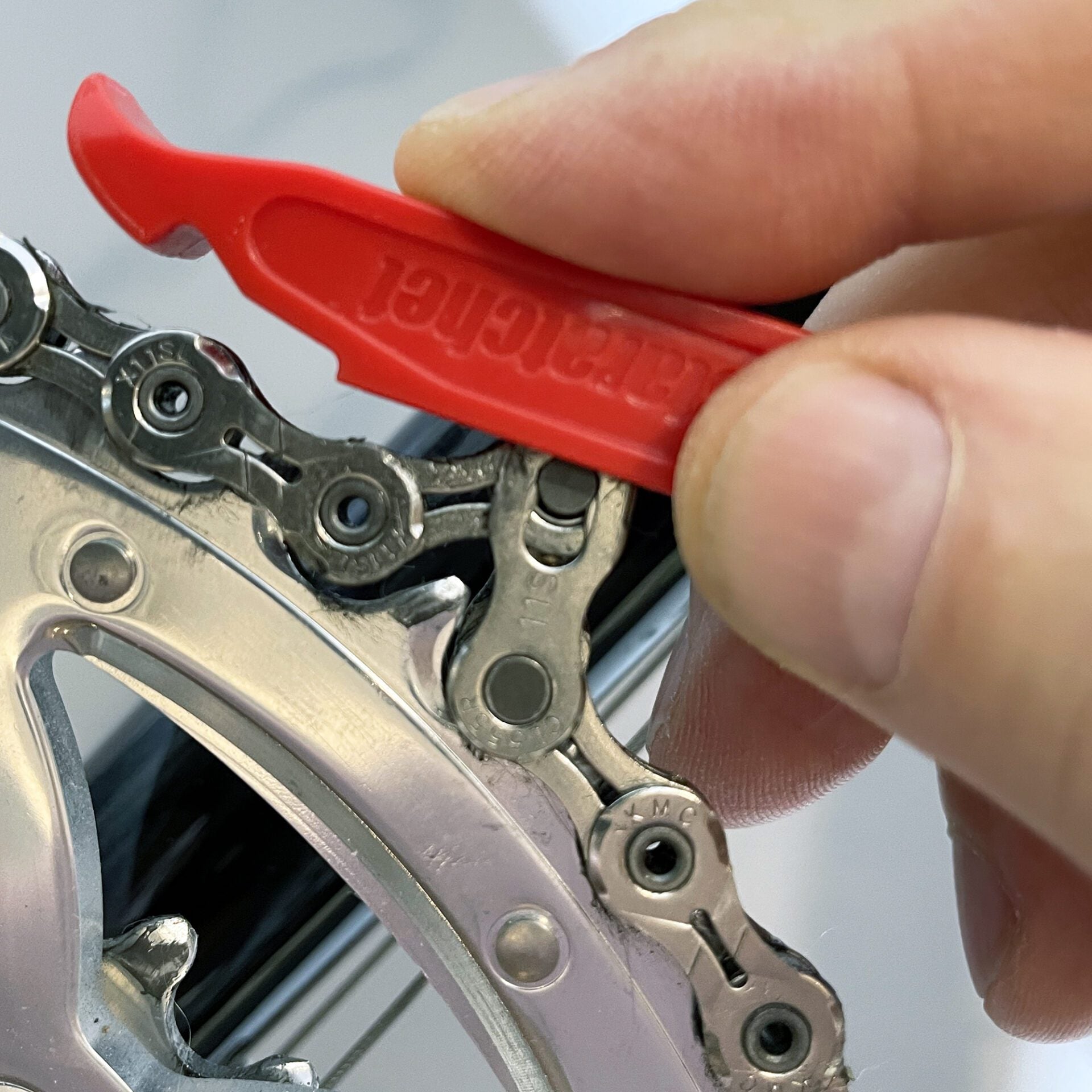 A close-up of a hand using the Prestaratchet GO - 5 tools-in-one Multi-tool Kit to check chain wear on a bicycle positioned on a silver gear.