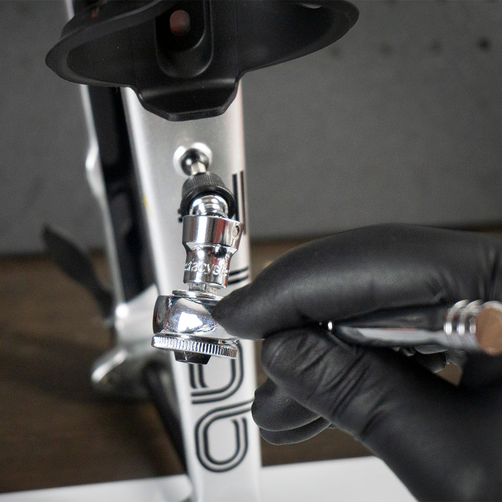 A person in a black glove uses an airbrush near a Colnago bike frame, while the Prestacycle Bits Swivel QR Torque Wrench Adapter by Prestacycle sits nearby, ready for precise adjustments after custom paintwork.