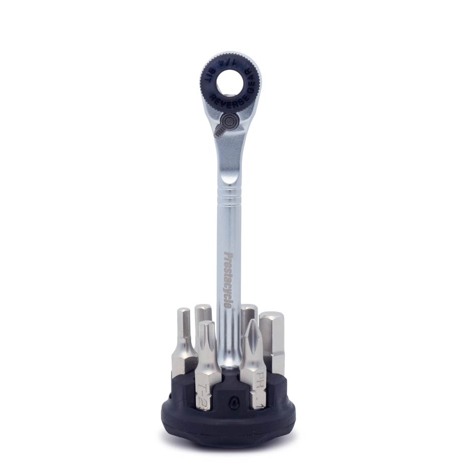 The Prestaratchet Micro – Kit features a small upright ratchet wrench in a black round holder, surrounded by six neatly arranged S2 1/4 bits at its base.