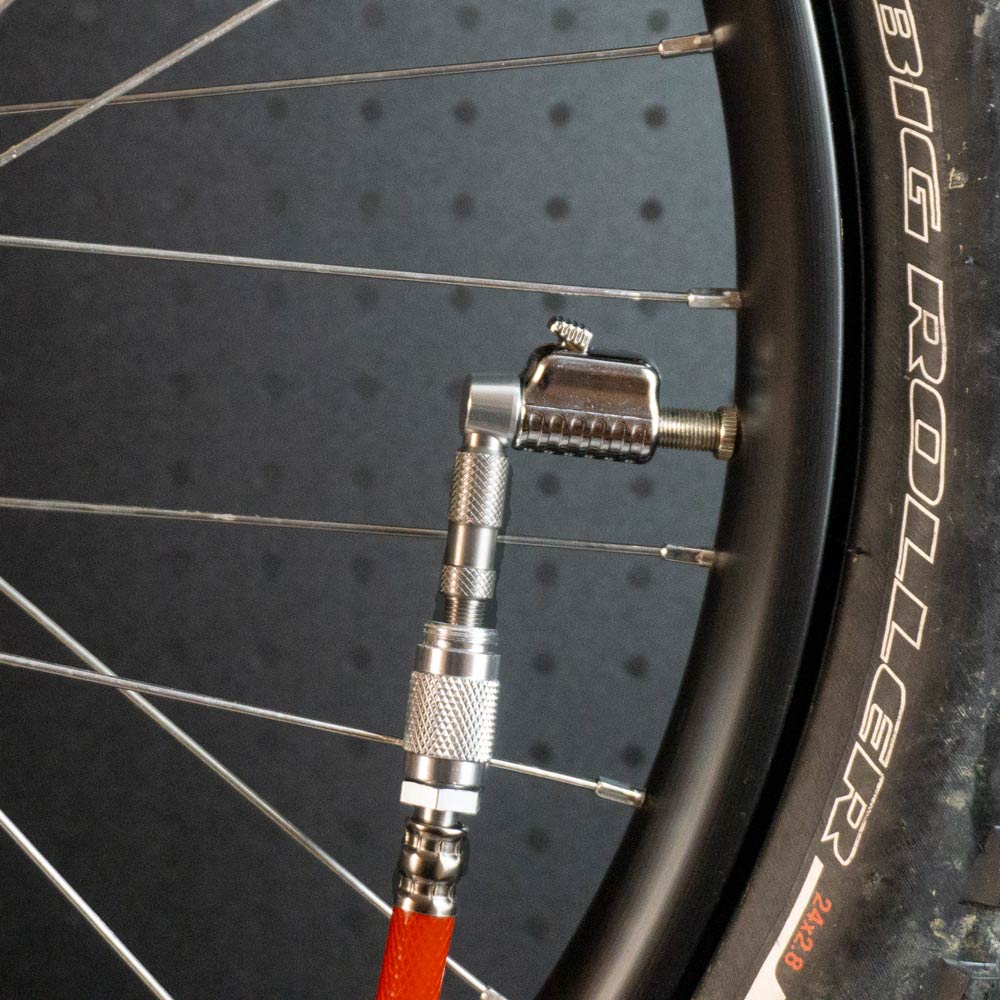 A close-up shows a bicycle tire labeled BIG ROLLER being inflated with a pump using the Prestacycle Pro Schrader Head nozzle, securely attached to the valve on the rim for optimal tire pressure.