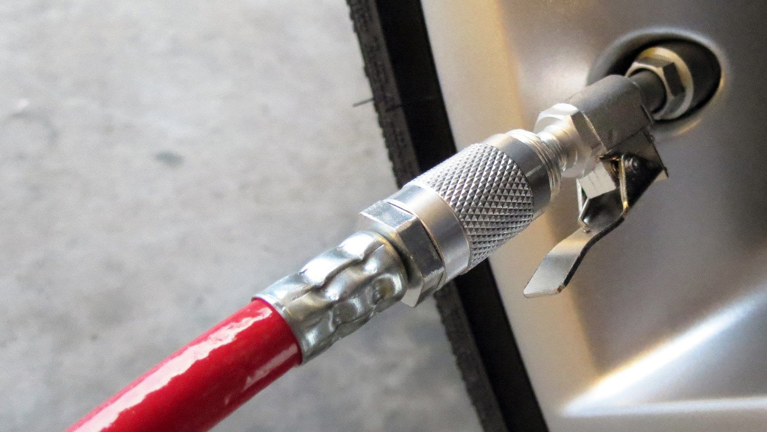 A close-up of the Prestaflator PRO Bicycle Tyre Inflator connected to a bike tire valve shows its secure metal connector with pressure checker. The red hose contrasts with the wheel rim, ensuring precise inflation for Presta &amp; Schrader valves.