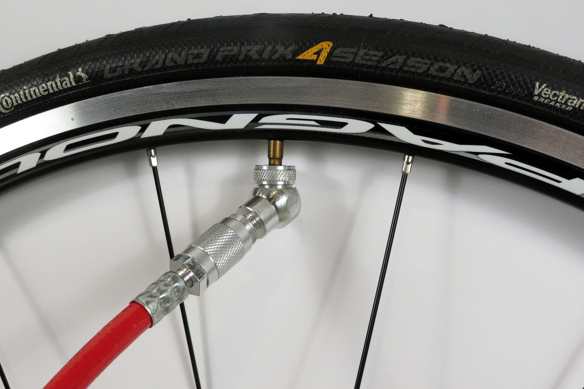 A close-up of a Continental Grand Prix 4 Season tubeless tire being inflated with a red air pump hose featuring the Prestacycle Angle Mini Presta Head attached to the valve. The tire branding is visible on the sidewall.